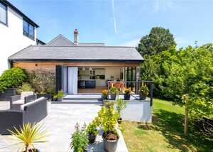 Modern home exterior with a patio, garden, and potted plants on a sunny day.